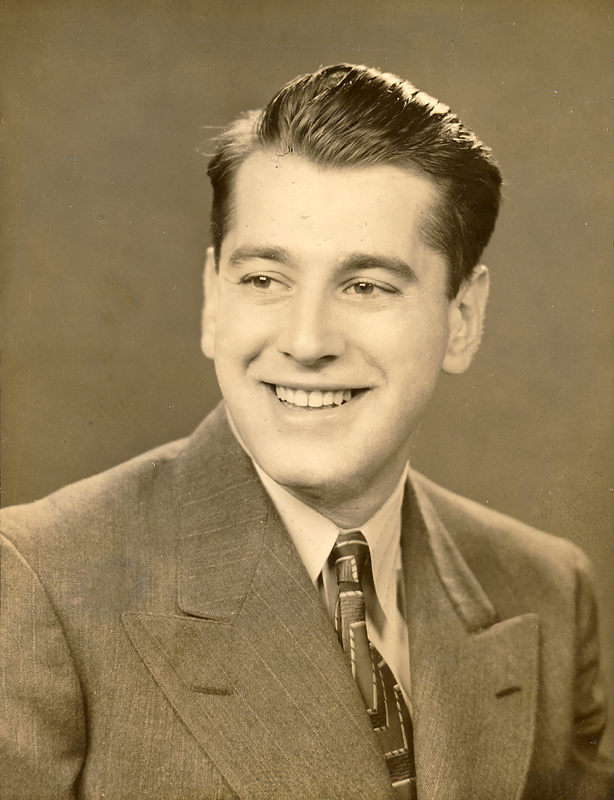 Portrait of Aaron Slom wearing a suit and tie, posing in front of a dark background.