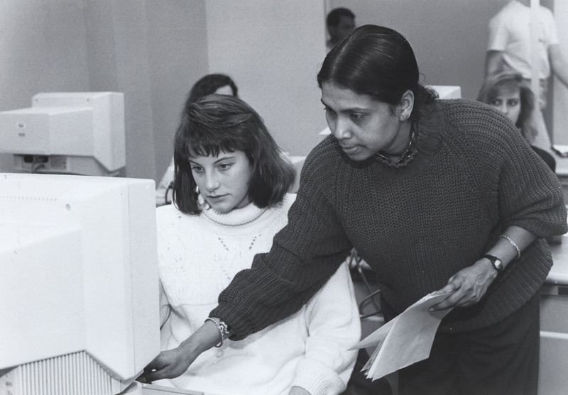 Nazma Latif-Zaman stands next to a student helping them with a computer.