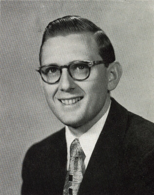 Portrait of Morton Pomerantz wearing glasses, a suit, and a patterned tie, smiling at the camera against a plain light background.
