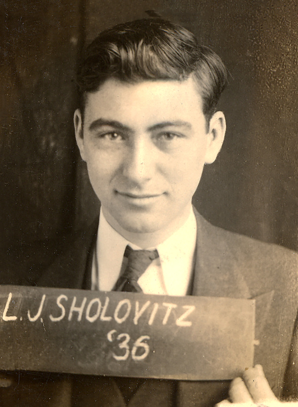 Leonard Sholovitz in a suit and tie holding a sign that reads 'L.J. Sholovitz '36,' looking directly at the camera.