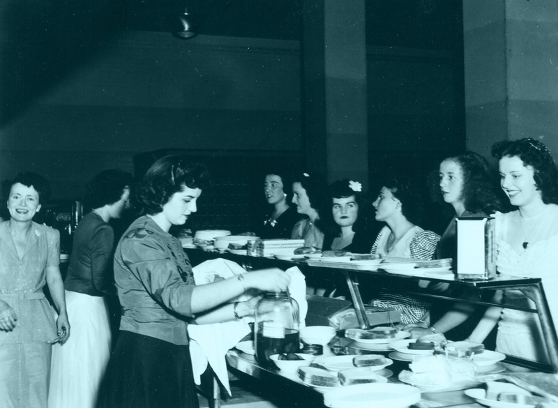 Several women in a cafeteria serving and being served food.
