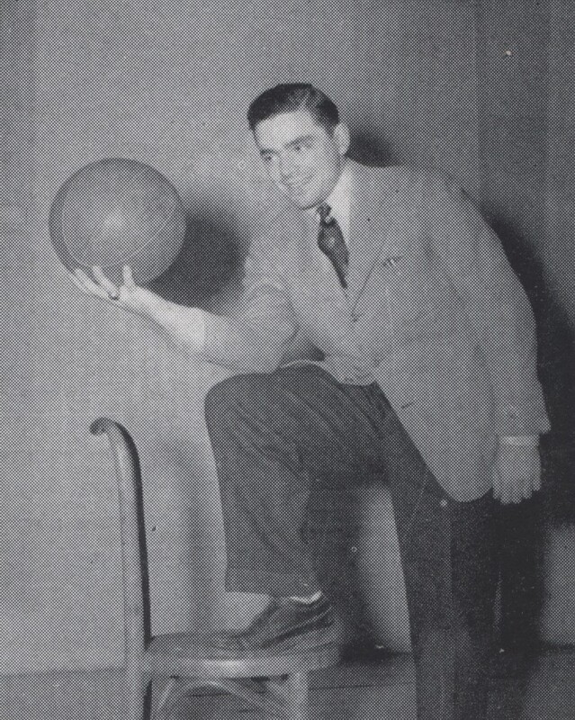 Portrait of Jerome Tesler in a suit posing with one foot on a chair, holding a basketball and smiling at the camera against a plain background.