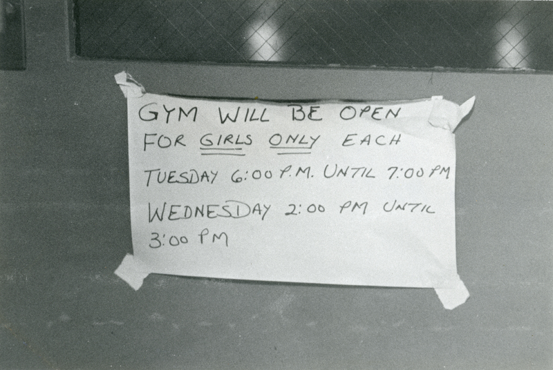 A piece of paper taped to a door that reads 'Gym will be open for girls only each Tuesday 6:00pm until 7:00pm Wednesday 2:00pm until 3:00pm.'