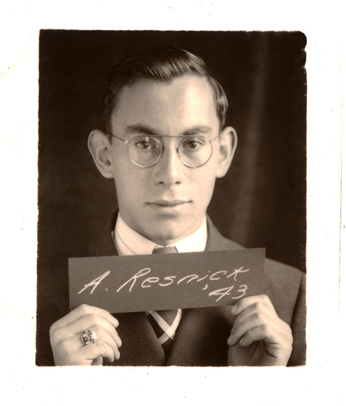 Portrait of Albert Resnick in glasses, suit, and tie holding a sign that reads 'A. Resnick, '43'.