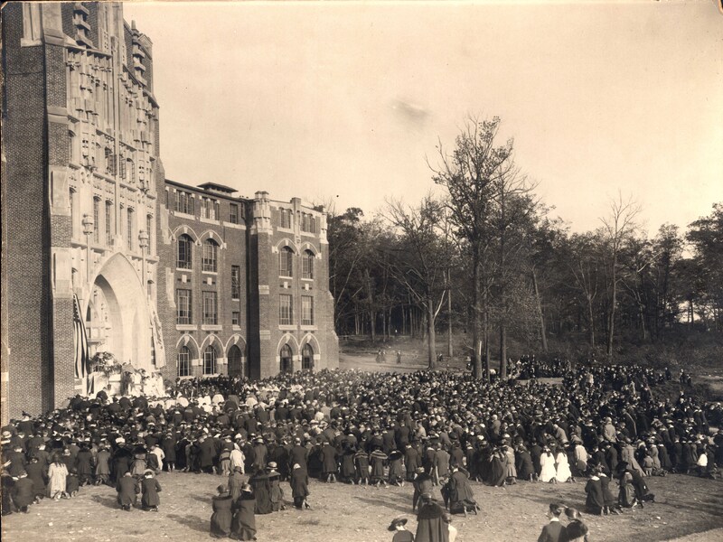 A large crowd gathered outside a Gothic-style building with arched windows and stonework, attending the Harkins Hall dedication.