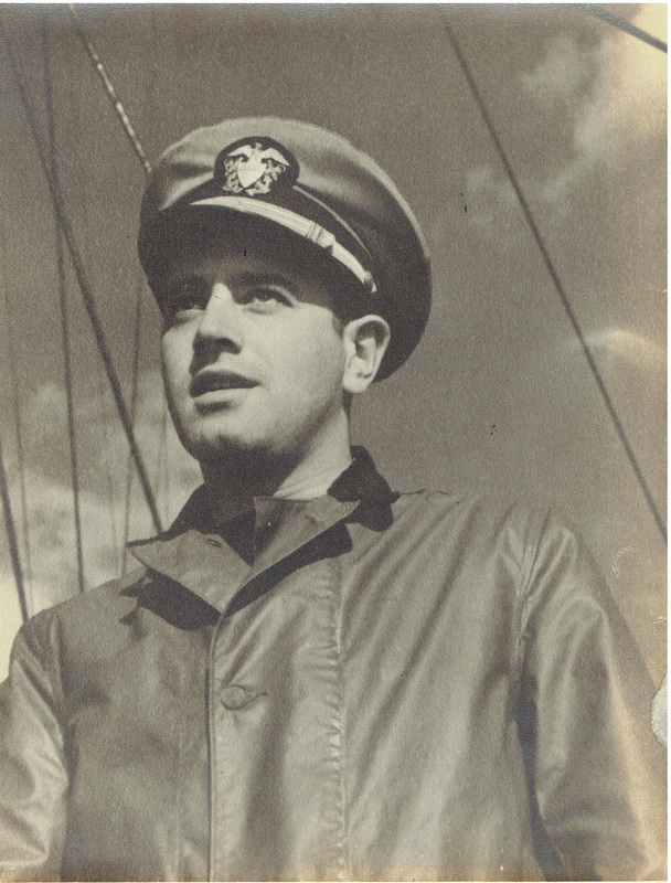 Photo of Aaron Slom in a military uniform and peaked cap, standing in front of ship rigging under a cloudy sky.