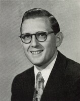 Portrait of Morton Pomerantz wearing glasses, a suit, and a patterned tie, smiling at the camera against a plain light background.