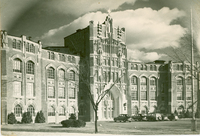 A Gothic-style building with arched windows and ornate stonework, vintage cars parked in front, and trees in the foreground.