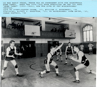 The 1934–1935 basketball team practicing in a gym with wooden floors, and spectators on an upper balcony.