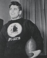 Aaron Slom standing indoors holding a football, wearing a dark sweatshirt with the word "Friars" and an image of a friar on the front, with curtains in the background.