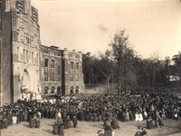 A large crowd gathered outside a Gothic-style building with arched windows and stonework, attending the Harkins Hall dedication.