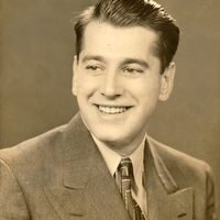 Portrait of Aaron Slom wearing a suit and tie, posing in front of a dark background.