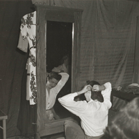 A woman sits on the floor of a dressing room in front of a mirror pinning her hair back.