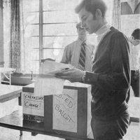 A student standing in front of a ballot box holding a piece of paper. The box reads 'Coed ballot' and 'Calendar change.' There are two other students in the background.