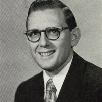 Portrait of Morton Pomerantz wearing glasses, a suit, and a patterned tie, smiling at the camera against a plain light background.