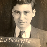 Leonard Sholovitz in a suit and tie holding a sign that reads 'L.J. Sholovitz '36,' looking directly at the camera.