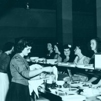 Several women in a cafeteria serving and being served food.