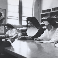 Four nuns are sitting at a table in a library reading from books.