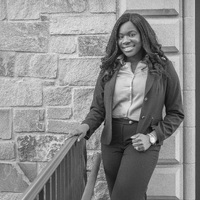 Taiwo Adefiyiju-Monwuba poses at the top of a set of stairs in front of a stone building.