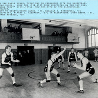 The 1934–1935 basketball team practicing in a gym with wooden floors, and spectators on an upper balcony.