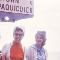 Three women pose outside for a photo standing beneath a sign that partially reads 'Chappaquiddick.'