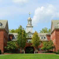 Large, symmetrical brick building with a central archway and clock tower, surrounded by trees and a lawn in the foreground.