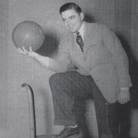 Portrait of Jerome Tesler in a suit posing with one foot on a chair, holding a basketball and smiling at the camera against a plain background.