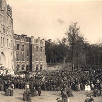 A large crowd gathered outside a Gothic-style building with arched windows and stonework, attending the Harkins Hall dedication.