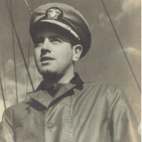Photo of Aaron Slom in a military uniform and peaked cap, standing in front of ship rigging under a cloudy sky.